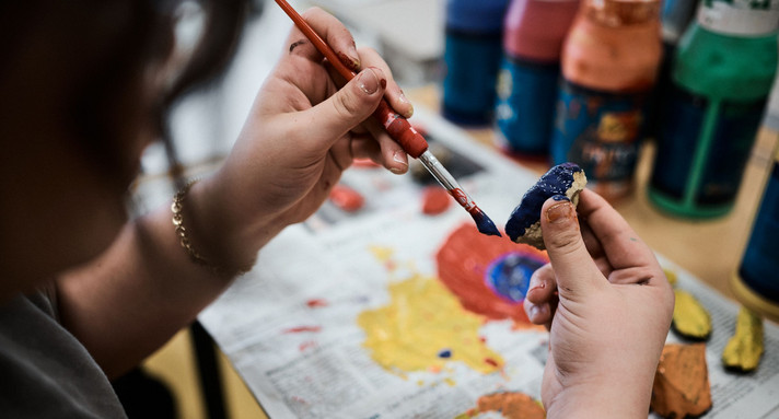 Schülerin bemalt mit Pinsel und blauer Farbe einen kleinen Stein