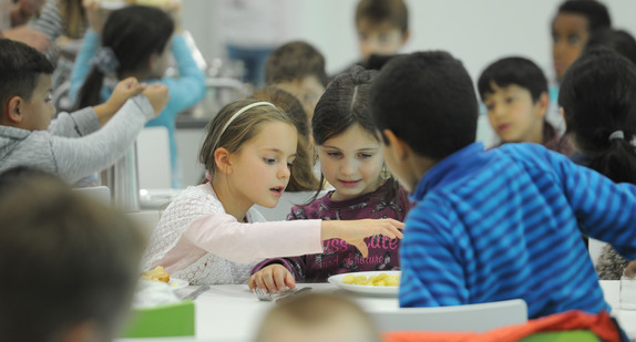 Guppe von jüngeren Schülerinnen und Schülern verschiedener Ethnien gemeinsam beim Mittagessen in der Schulkantine