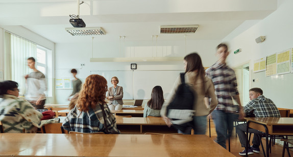 Eine Klasse mit jugendlichen Schülerinnen und Schülern von hinten aufgenommen, vorne am Whiteboard steht eine Lehrerin