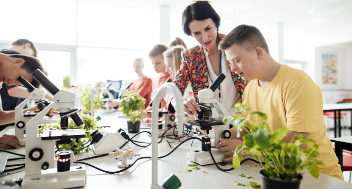 Down-Syndrom-Junge in der Schule, inklusives Lernen im Labor mit einem Mikroskop, Lehrerassistenz.