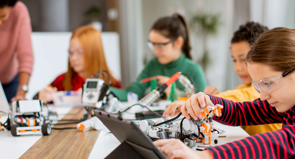 Schülerinnen und Schüler arbeiten mit einer Lehrerin an selbstprogrammierten Robotern