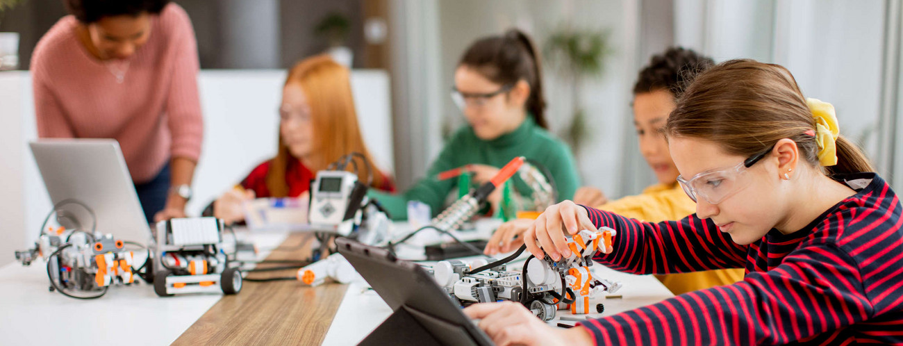 Schülerinnen und Schüler arbeiten mit einer Lehrerin an selbstprogrammierten Robotern