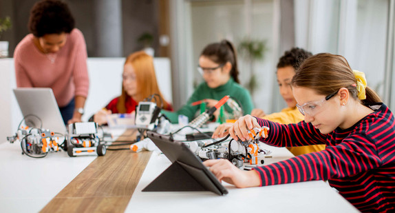 Schülerinnen und Schüler arbeiten mit einer Lehrerin an selbstprogrammierten Robotern