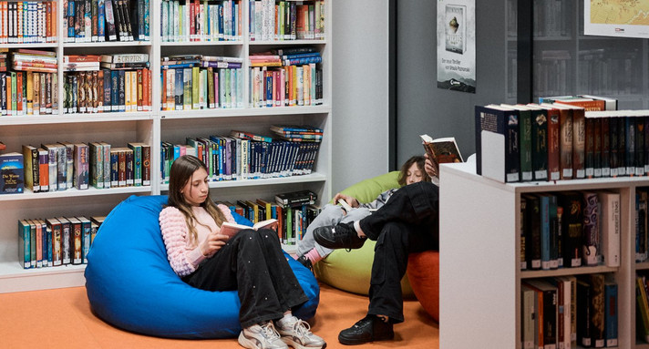 Zwie Kinder sitzen in einer Bücherei auf Sitzsäcken und lesen
