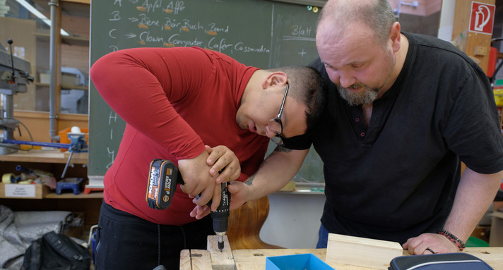 Lehrer gibt älteren Schüler mit Behinderung Hilfe beim Erlernen von Arbeiten mit einem Akkuschrauber