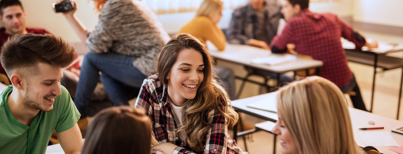 Lächelnde Schülerinnen und Schüler genießen die Pause im Klassenraum und kommunizieren.