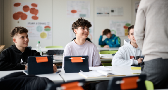 Schüler mit Tablets lauschen aufmerksam einer Lehrkraft
