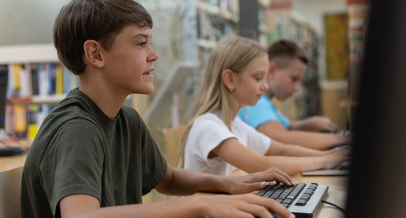 Kinder in einer Schulbibliothek vor Computern am Arbeiten