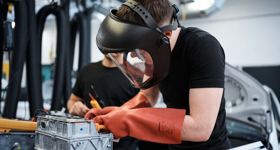 Ein Junge mit Schutzbrille und Handschuhen in einer Autowerkstatt