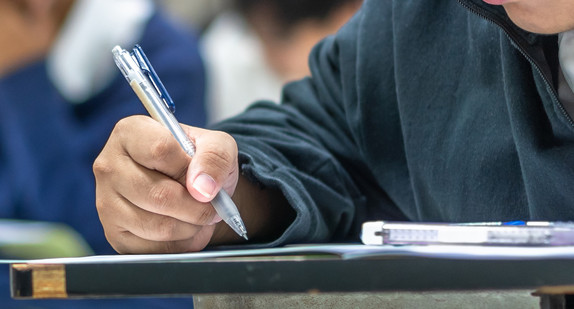 Junger Mann schreibt Prüfung. Zu sehen ist vor allem seine Hand und ein Teil des Oberkörpers