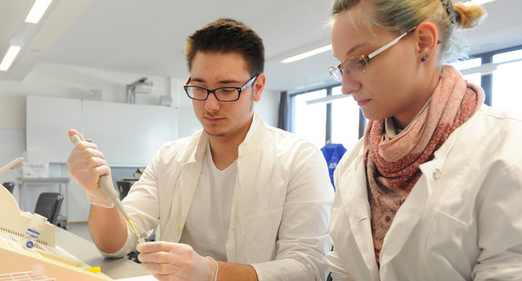 Eine Schülerin und ein Schüler arbeiten mit weißen Kitteln im Labor