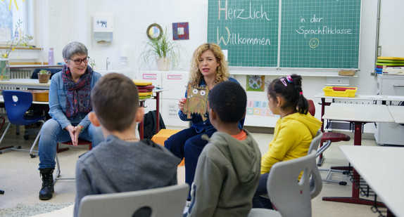 Zwei Lehrerinnen sitzen mit Kindern in einem Klassenzimmer im Stuhlkreis
