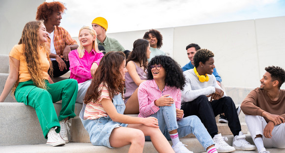 Glückliche verspielte multiethnische Gruppe junger Freundinnen und Freunde, die im Freien auf einer Treppe sitzen.