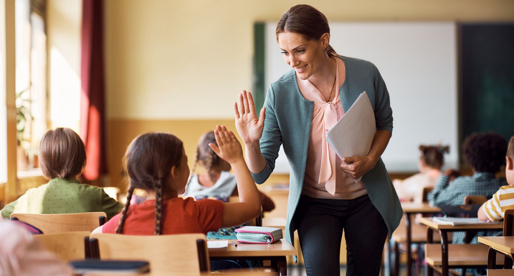 Eine Lehrerin im Klassenzimmer mit Kindern gibt einer Schülerin High-Five.