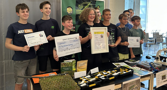 Gruppenbild der Gewinnerinnen und Gewinnern des NANU?!-Wettbewerbs 2026 mit ihren Preisen an ihrem Stand.