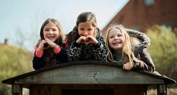 Drei Kinder lehnen sich über das Dach eines Holzhauses. 