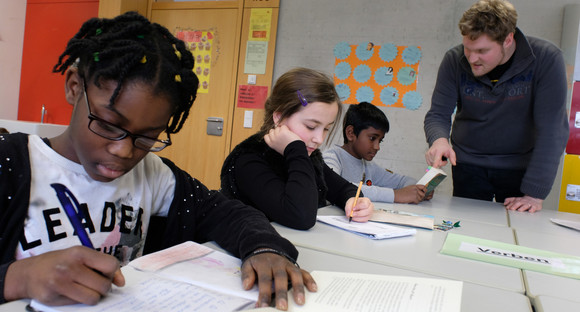 Lehrer hilft drei Schülerinnen und Schülern unterschiedlicher Ethnien bei Aufgaben