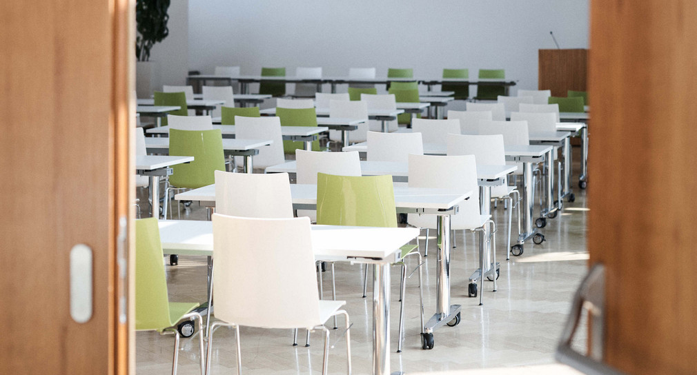 Blick durch eine Tür in einen Schulraum mit Tischen und Stühlen
