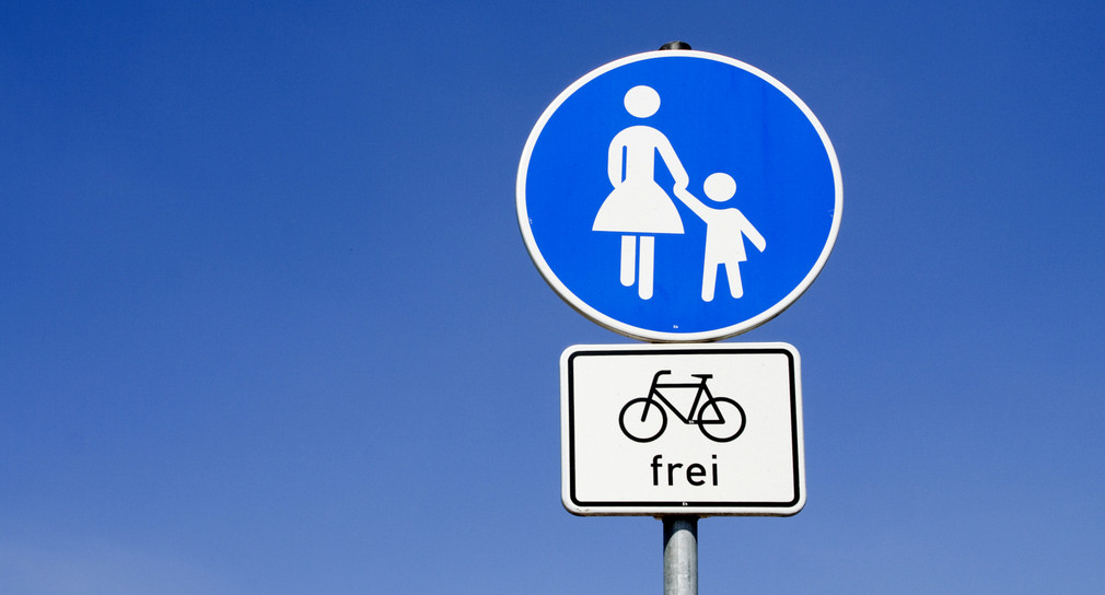 Zwei Verkehrsschilder übereinander vor einem blauen Himmel. Das obere Schild bedeutet Gehweg, das untere Schild für Fahrräder frei.