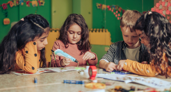 Gruppe verschiedener Kinder, die mit einem elektronischen Konstrukteur spielen und ein digitales Gerät im Klassenzimmer verwenden. 