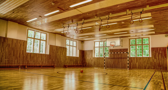 Eine leere Sporthalle mit Toren und Seilen. Aus den Fenstern dringt Licht hinein.