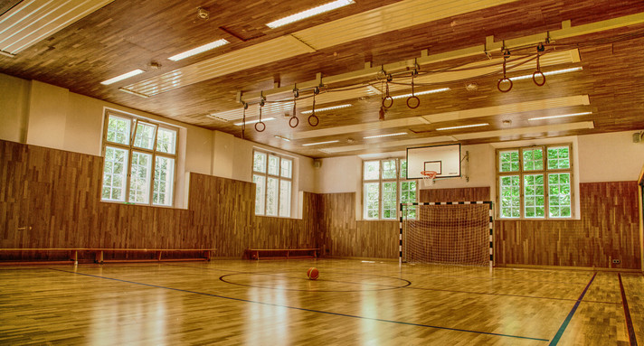 Eine leere Sporthalle mit Toren und Seilen. Aus den Fenstern dringt Licht hinein.