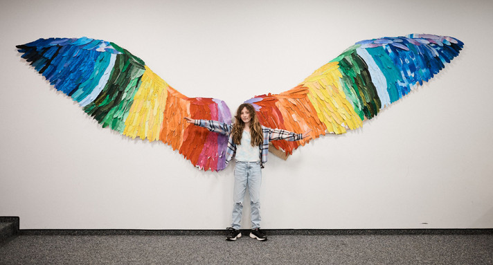 Mädchen steht vor einem Wandbild aus gemalten, bunten, Flügeln.