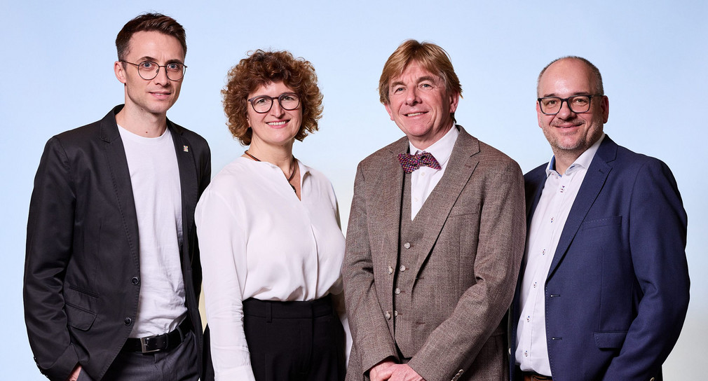 Drei Männer und eine Frau vor blauem Hintergrund