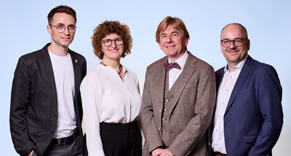 Drei Männer und eine Frau vor blauem Hintergrund