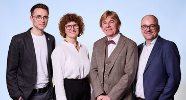 Drei Männer und eine Frau vor blauem Hintergrund