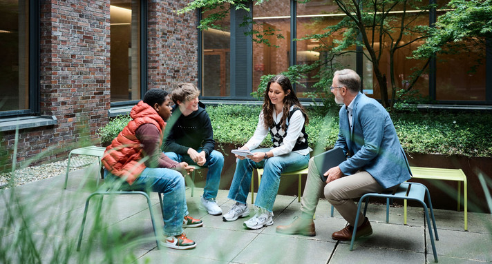 Schüler und Lehrer unterhalten sich auf einer Bank im Hof.