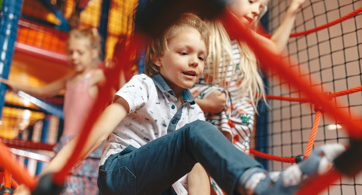 Zwei Schülerinnen und ein Schüler in einem Klettergerüst mit Seilen am Klettern