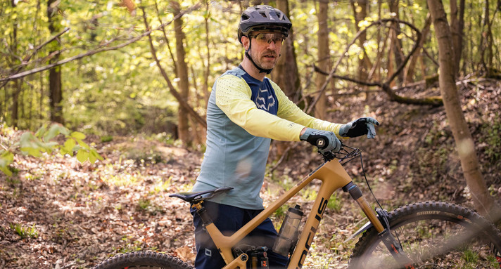 Ein Mann steht hinter einem Fahrrad mitten in einem Wald, er hat einen Fahrradhelm auf.  