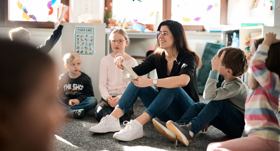Eine Frau sitzt von vier Kindern umringt auf dem Boden. 