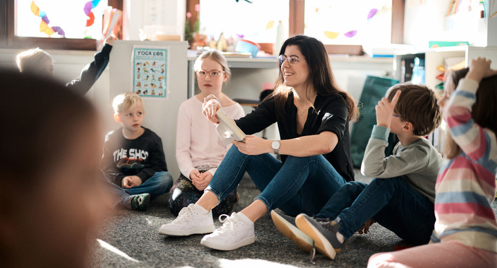 Eine Frau sitzt von vier Kindern umringt auf dem Boden. 