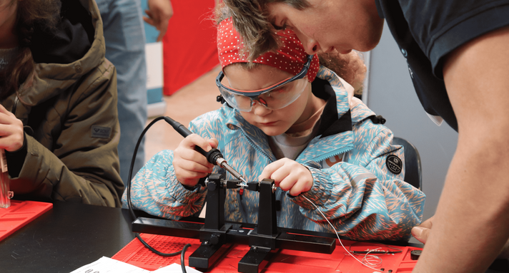 Eine Schülerin sitzt an einem Tisch und tüftelt mit physikalischen Geräten.
