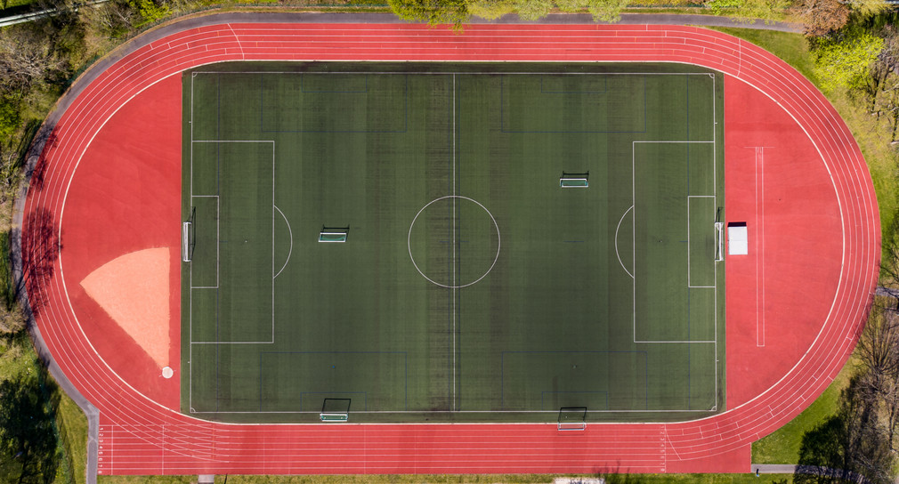 Sportstätten Bundesprogramm „Sanierung kommunaler Sportstätten“ Eine Aufnahme von oben auf einen grünen Fussballplatz, der umrandet ist von einer roten Laufbahn.