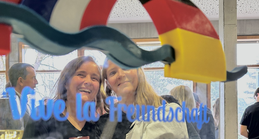 Zwei Frauen hinter einer Glaswand, auf der die deutsche und die französische Flagge zu sehen sind.