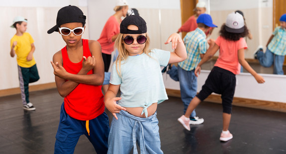 Mädchen und Junge in Mützen und Sonnenbrille bei Hip-Hop beim Gruppentanzkurs