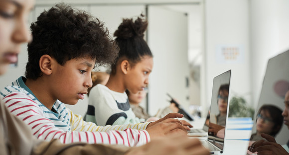 Multiethnische Kinder im Teenageralter sitzen vor Computern