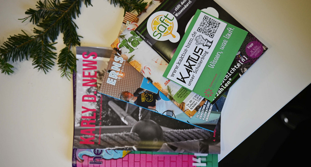 Verschiedene Schülerzeitschriften und ein Tannenzweig liegen auf einem Tisch.