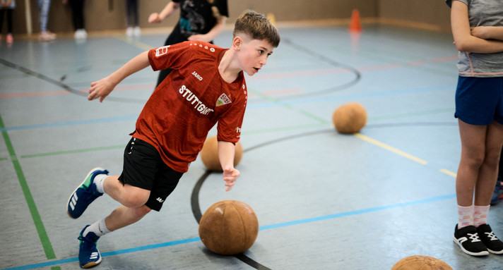 Ein Junge rennt in einer Sporthalle einem Ball hinterher. 