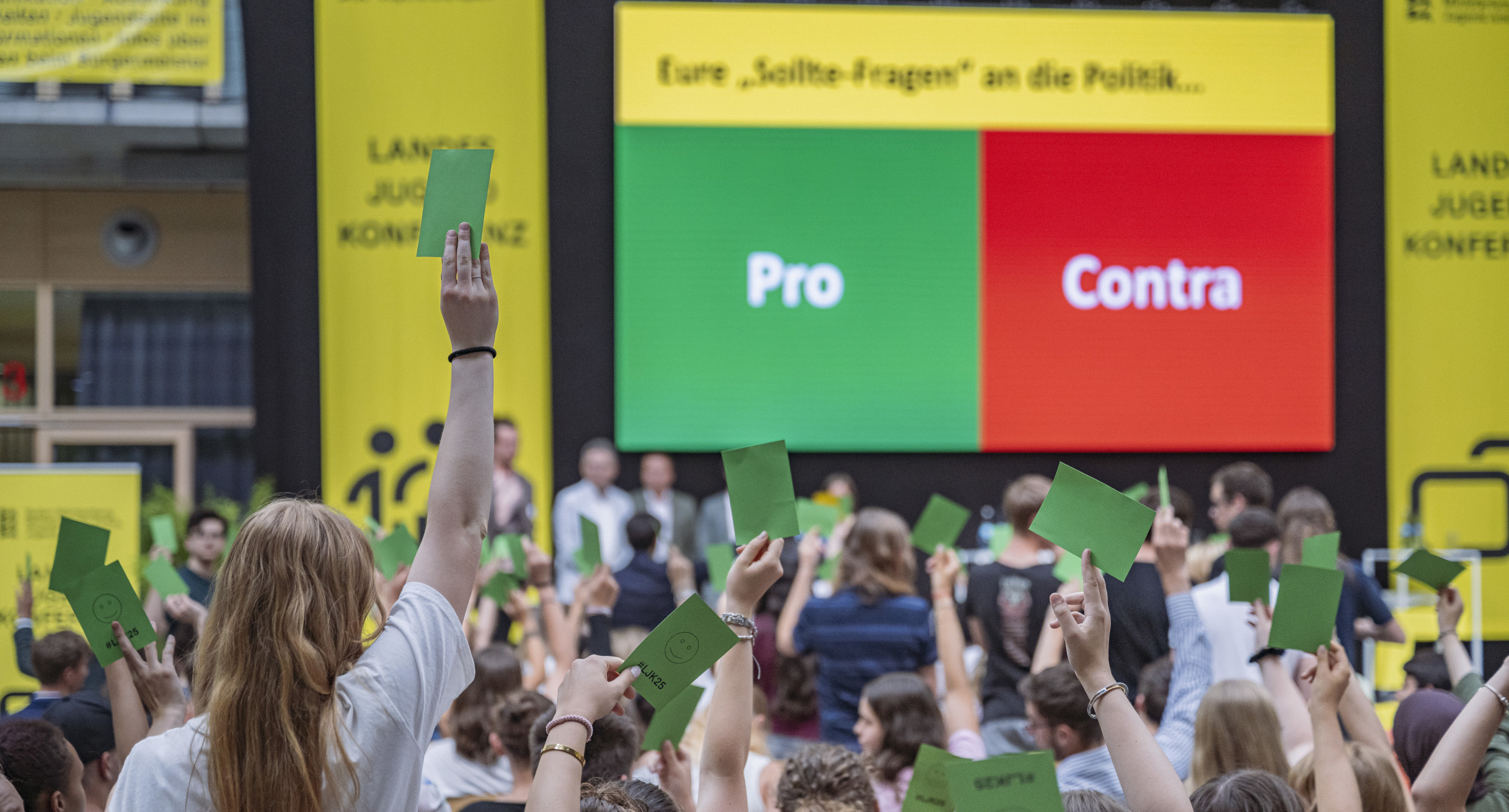 Auf einer Leinwand sind ein grüner und ein roter Balken zu sehen, davor hält eine Frau einen grüne Zettel in die Höhe. 